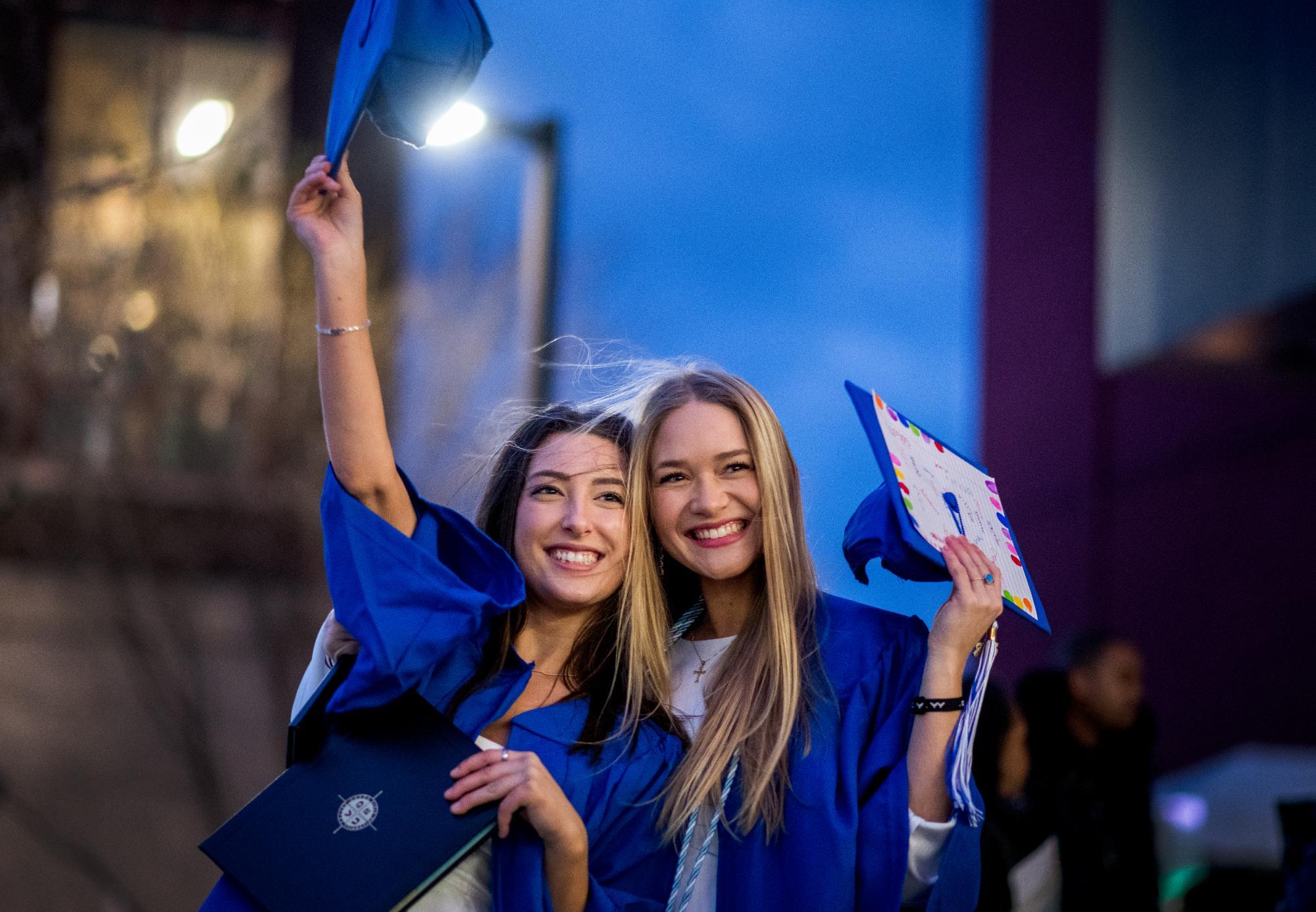 Two graduates wearing blue caps and smiling and celebrating at Commencement